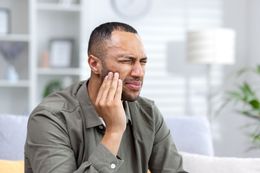 Tooth extraction: dental tool gripping a tooth above gums and two remaining teeth.