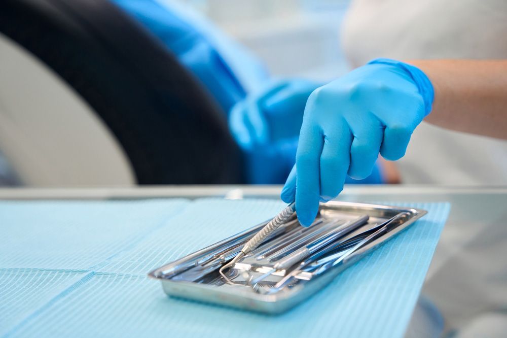 Person wearing blue gloves selects dental tool from a tray in a dentist's office.