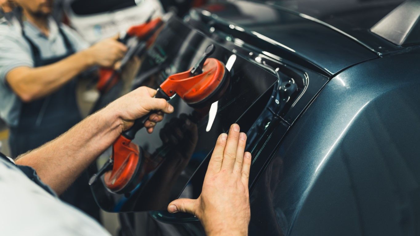 Workers installing a tinted car window with suction cups in a workshop.