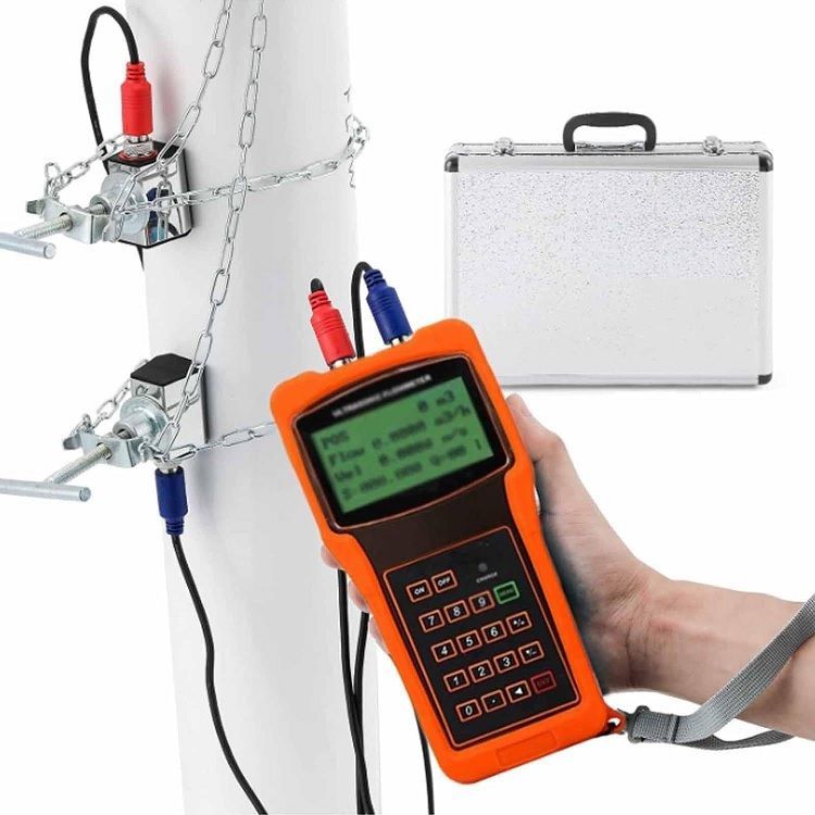 Mano sosteniendo un caudalímetro ultrasónico naranja, conectado a una tubería mediante sensores.