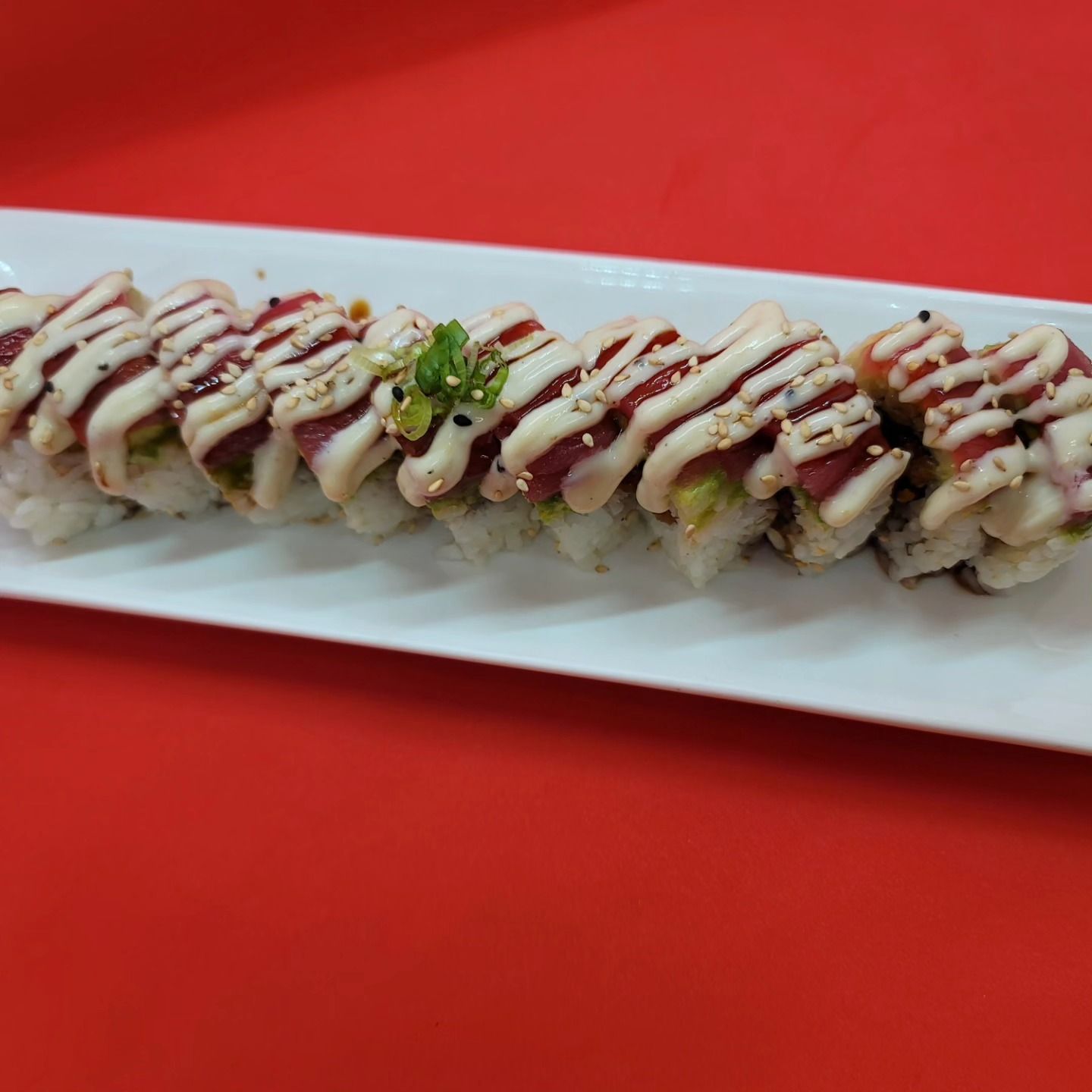 A row of sushi rolls on a white plate on a red table