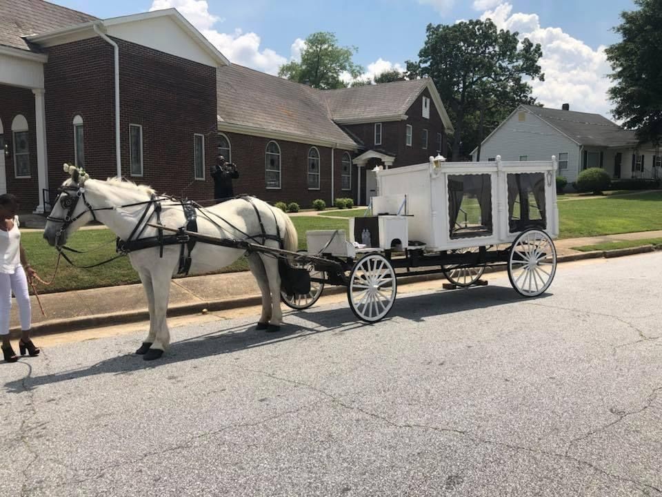 White horse-drawn hearse outside a brick church on a sunny day.