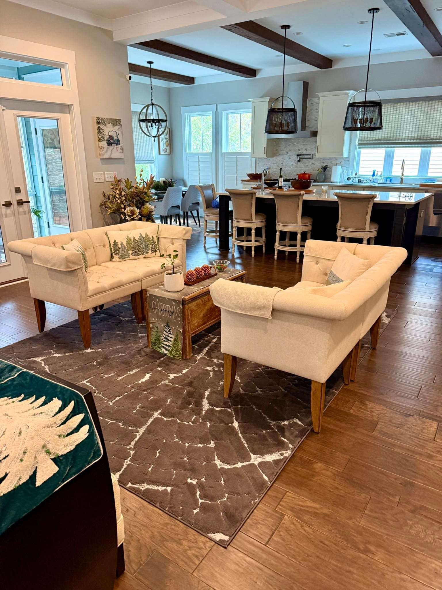Living room with two cream-colored sofas, rug, wooden floors, and an open kitchen with a bar.