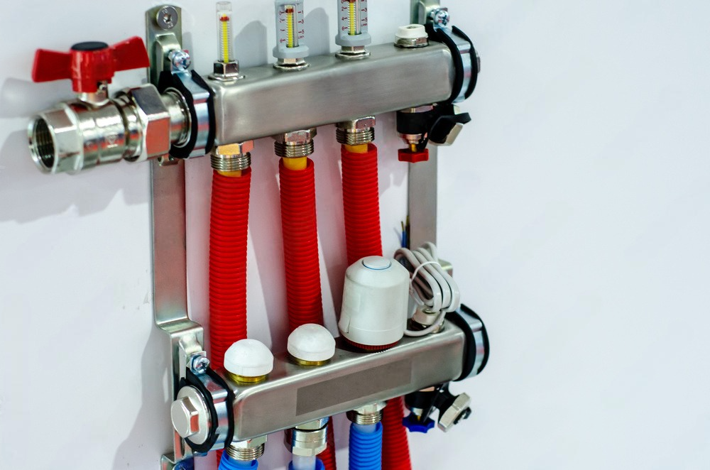 A stainless steel manifold with red hose and valves attached to it.