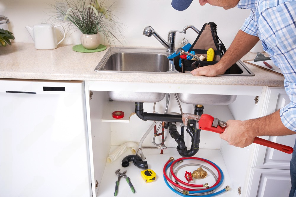 A plumber is fixing a sink in a kitchen with a wrench.