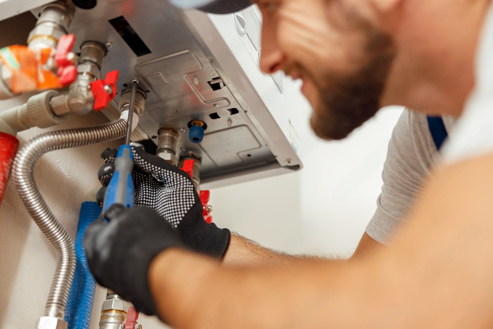 A man is fixing a boiler with a wrench.