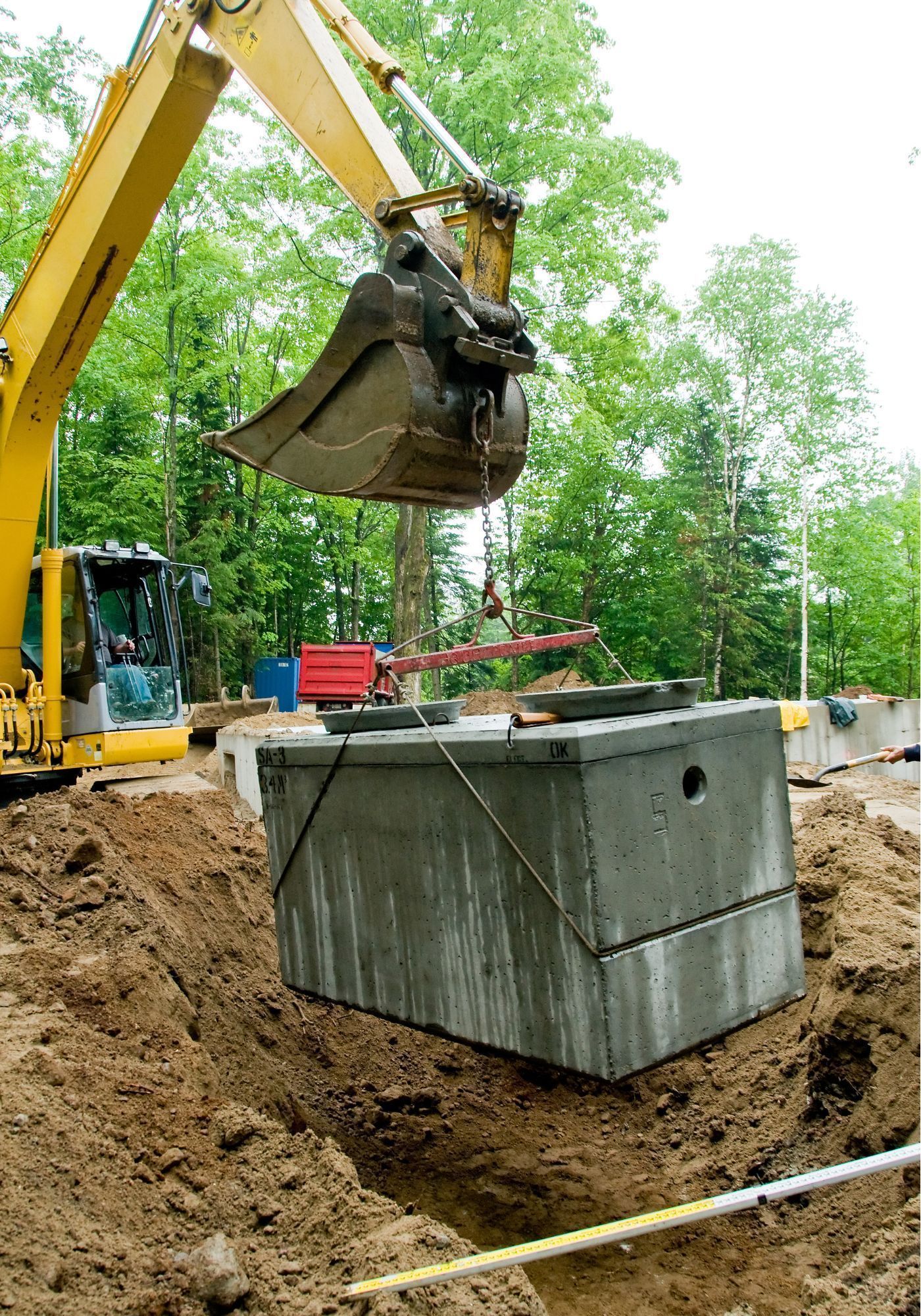 Black plastic water meter, partially buried in a trench, with open lid and connecting pipes.