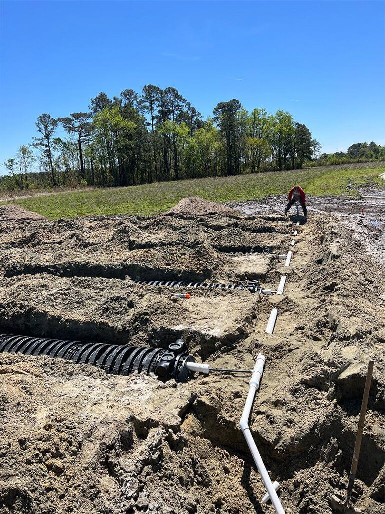 Construction site with trenches, pipes, and a worker in a red shirt. 