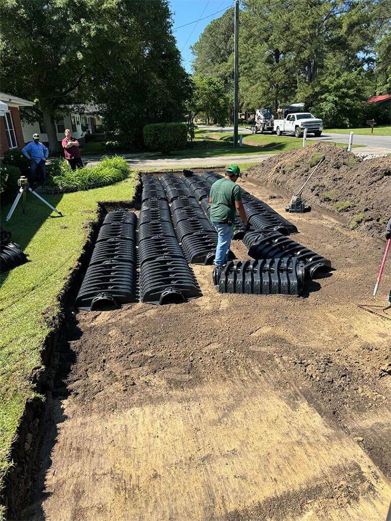 Man installing black drainage system in a yard. 