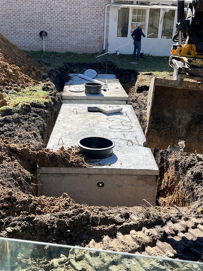 Excavated septic tank being installed near a house.