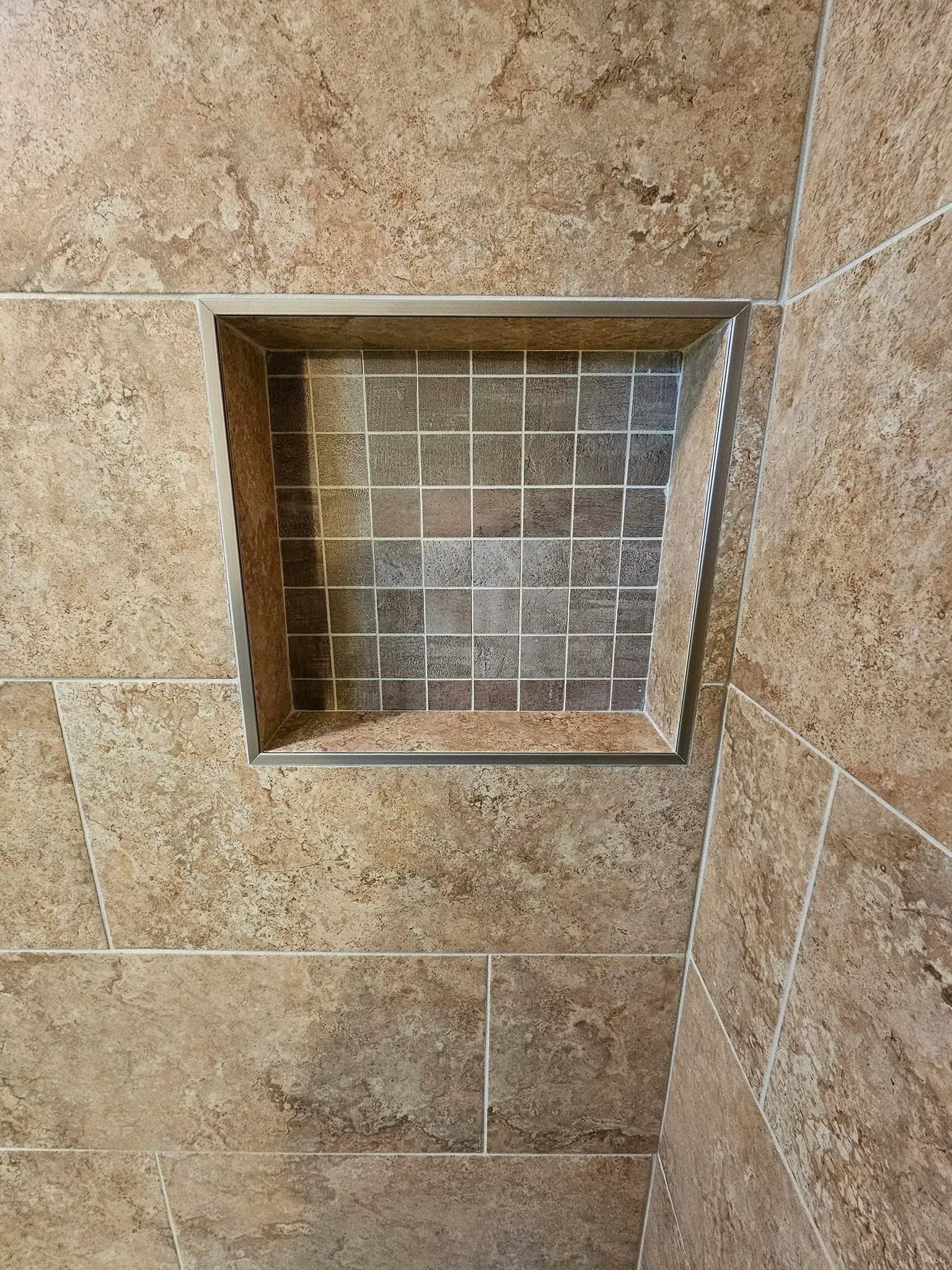 Tile shower niche with a rectangular opening lined with mosaic tiles, set in a stone-like tiled wall.