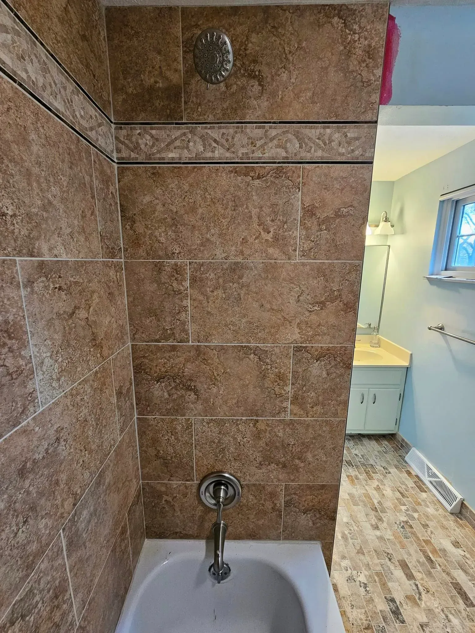 Bathroom interior with brown tiled shower, white tub, and sink in a light blue room.