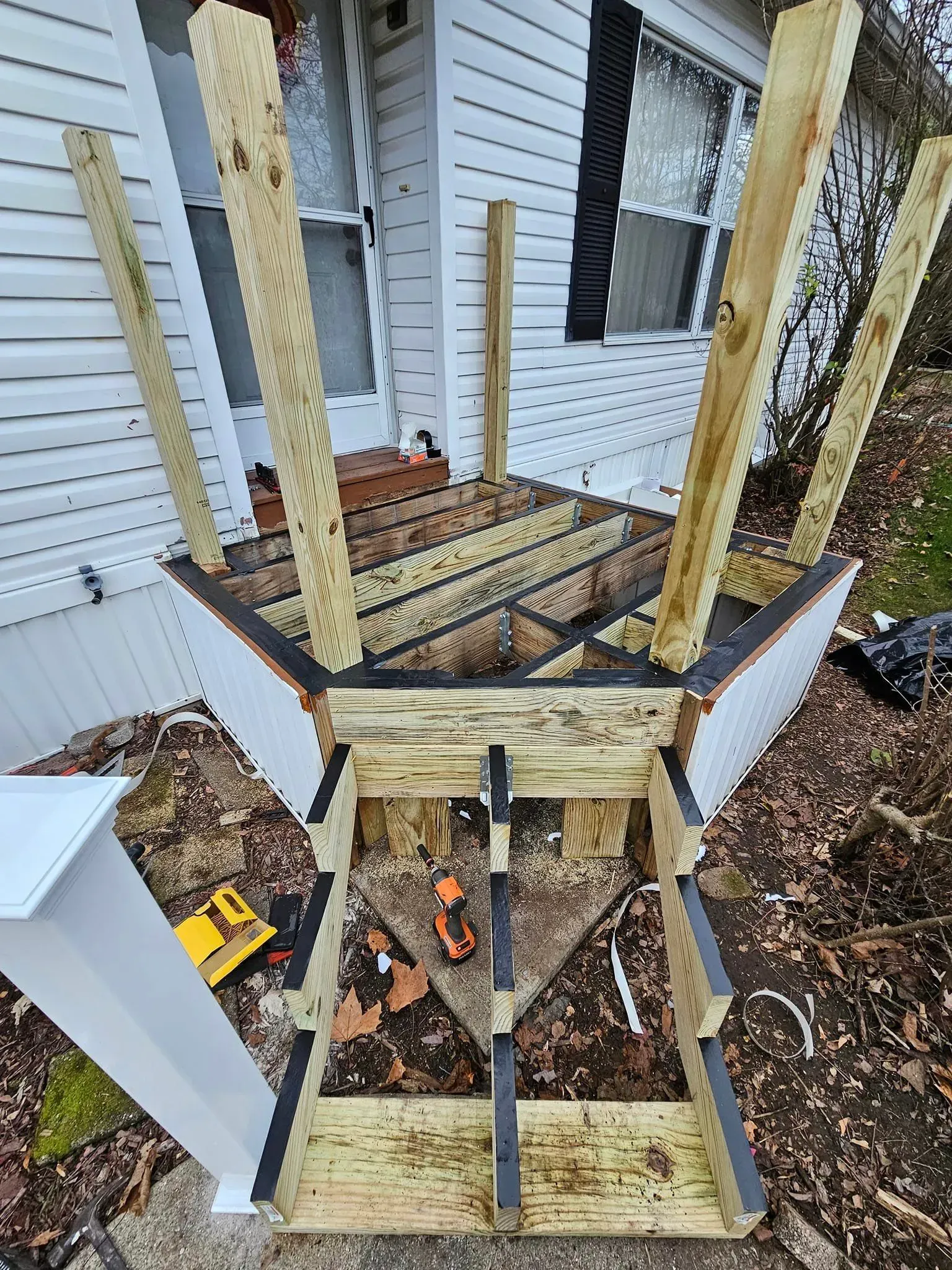 A wooden deck under construction outside a house with support beams extending upwards.