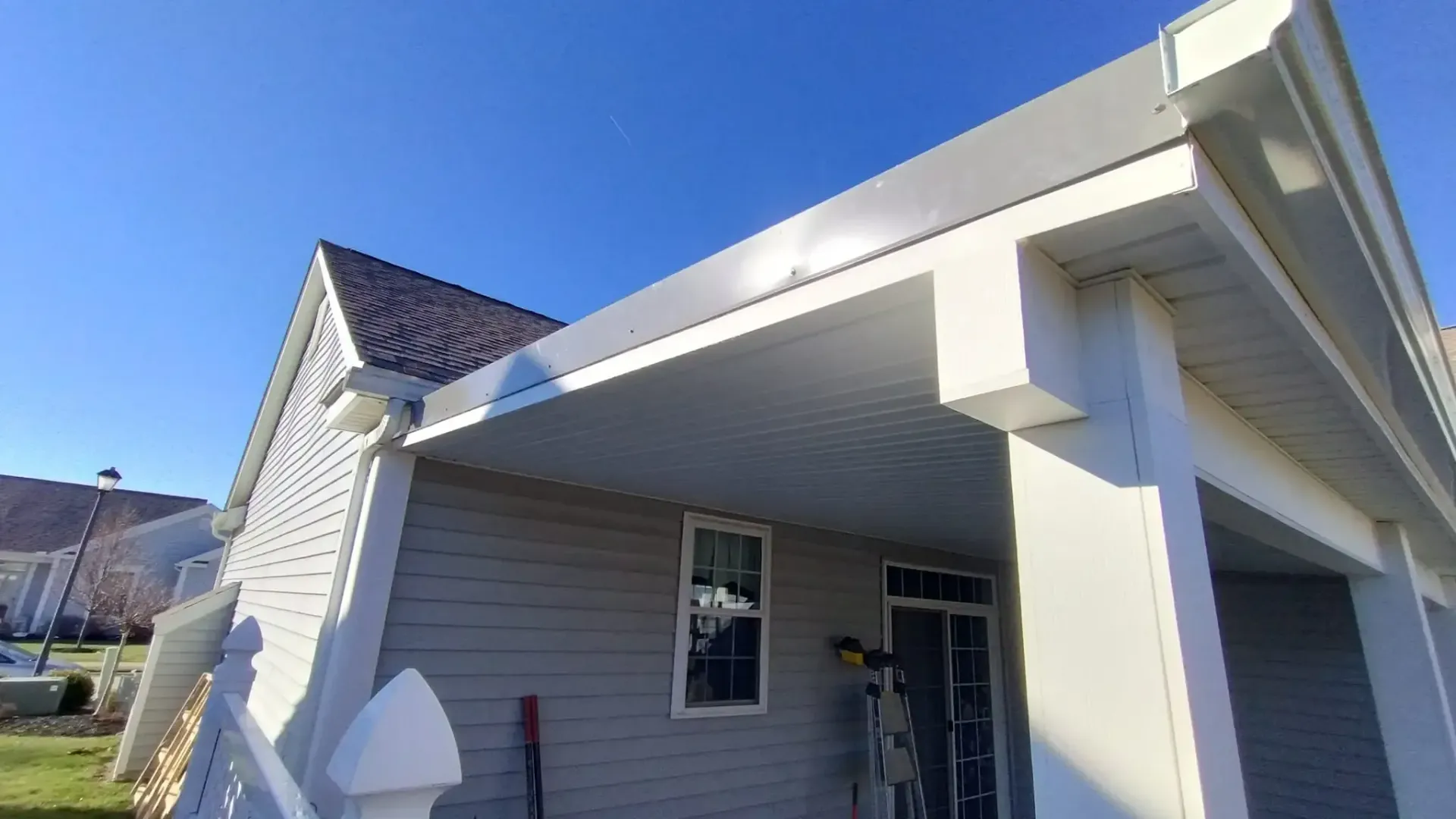 House exterior with gray siding, porch with white columns, and a dark roof on a sunny day.