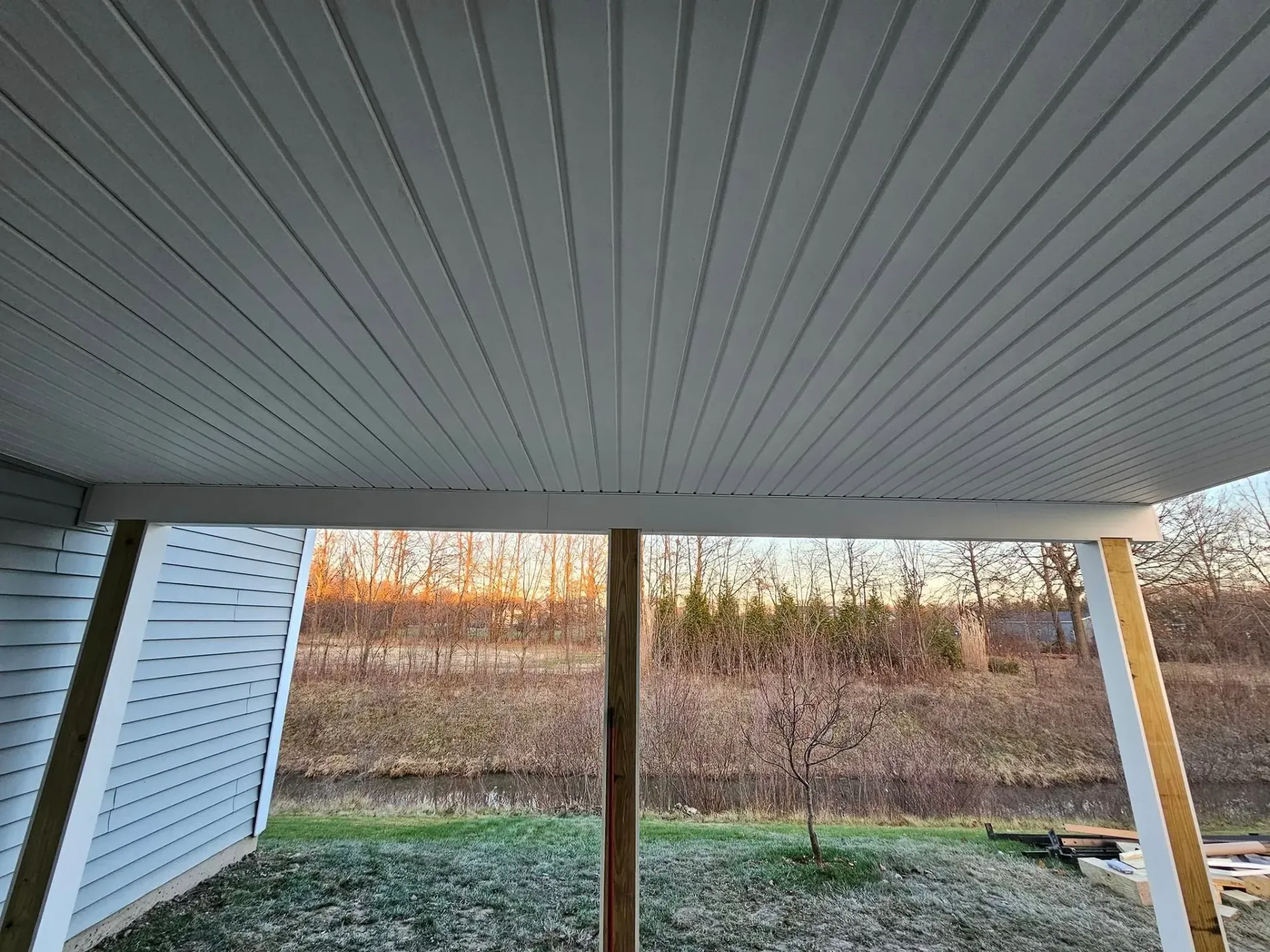 View from beneath a white porch roof, looking out at a yard with trees and ground cover.