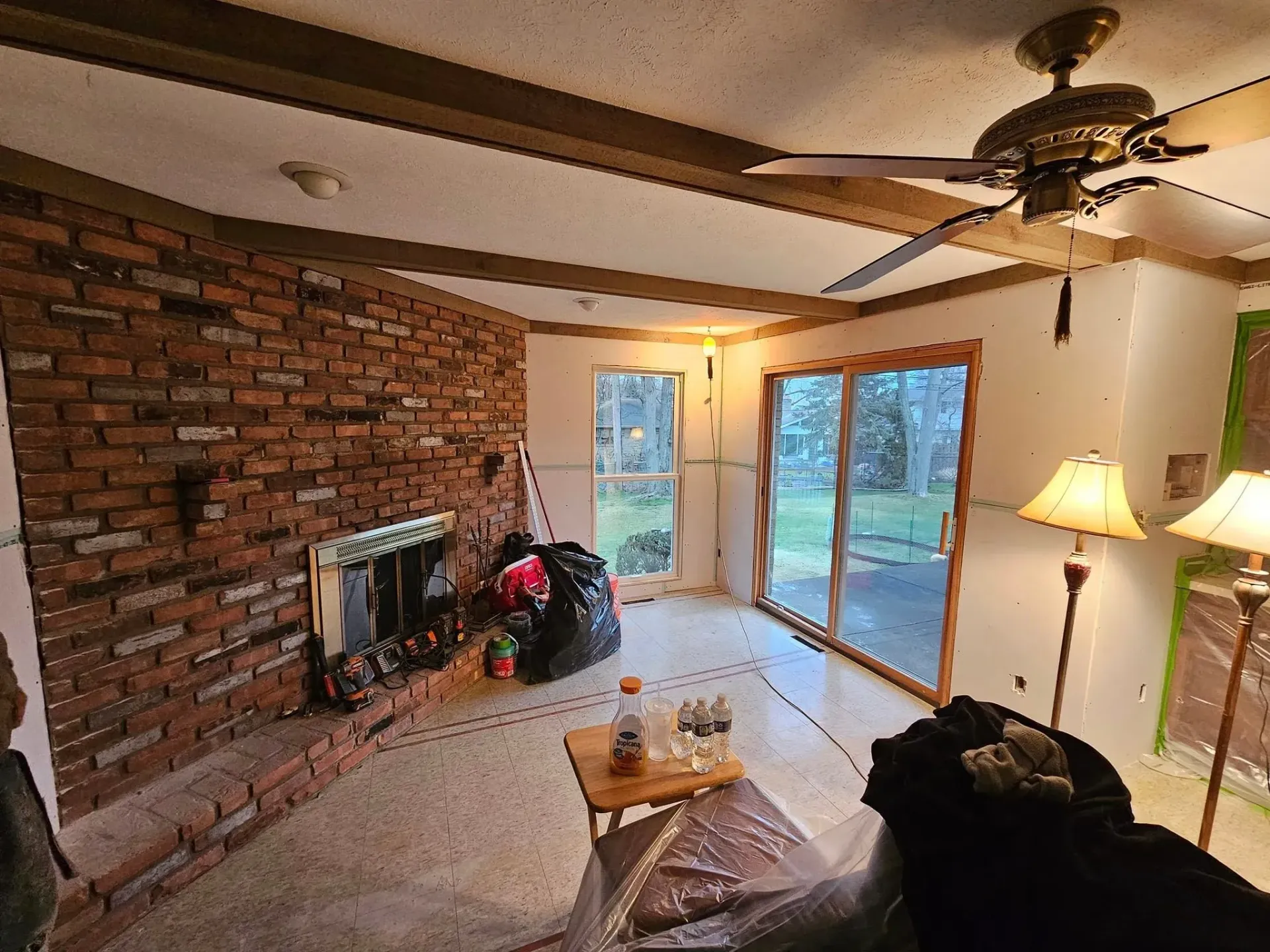 Brick-walled living room with fireplace, sliding glass door, and exposed ceiling beams; under renovation.