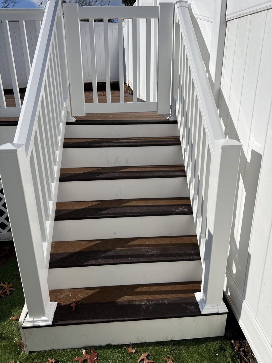 A set of deck stairs leading up to a deck with a white railing and a gate.