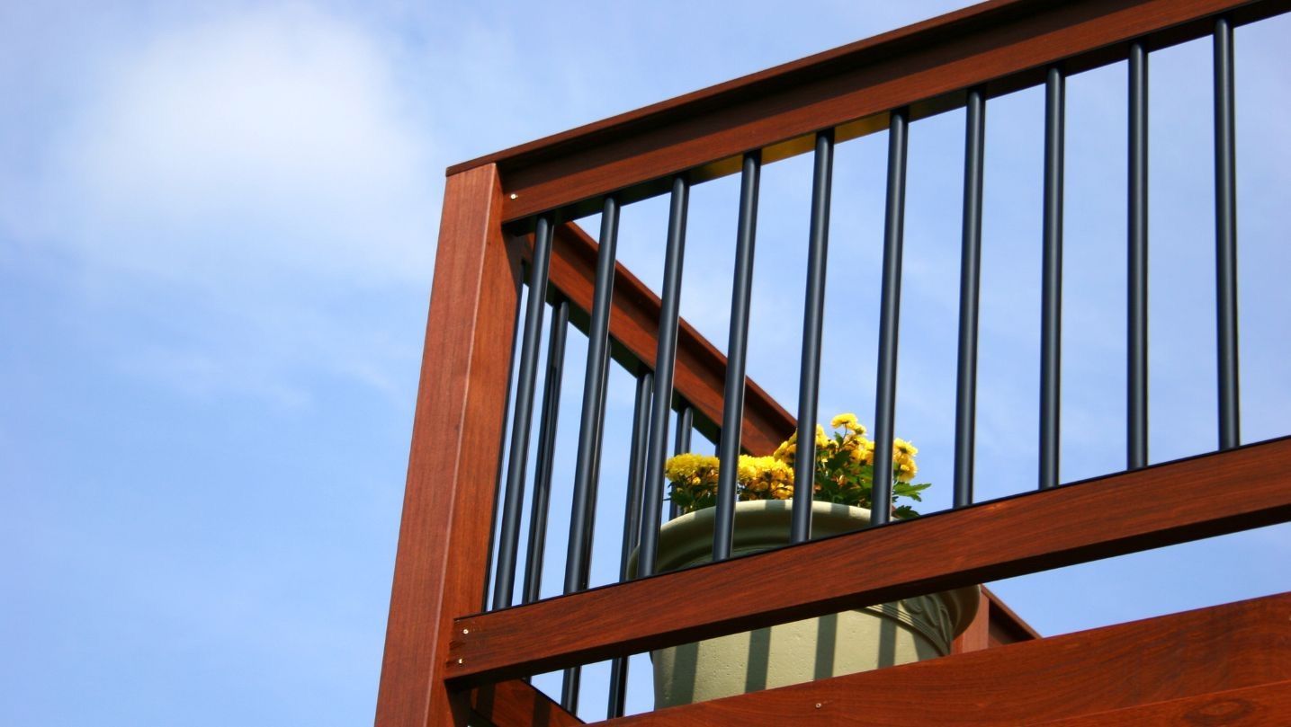 A wooden deck railing with a pot of yellow flowers behind it