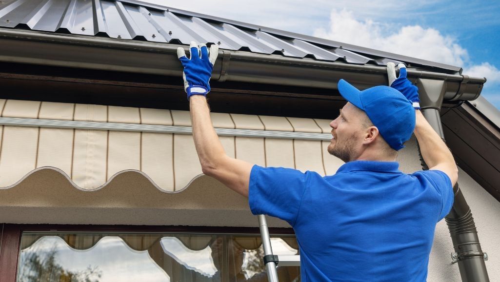 A man is fixing a gutter on the roof of a house.