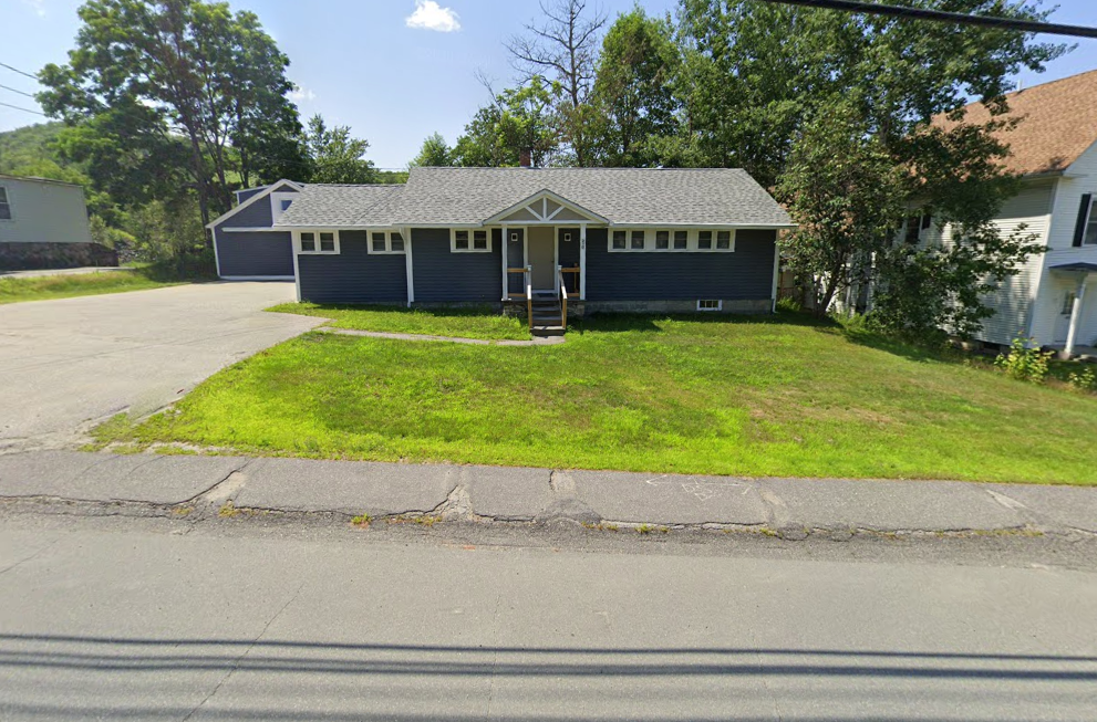A blue house with a gray roof sits on the side of the road