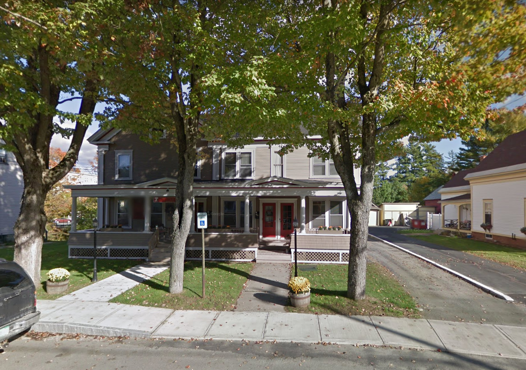 A house with a red door is surrounded by trees on the side of the road.