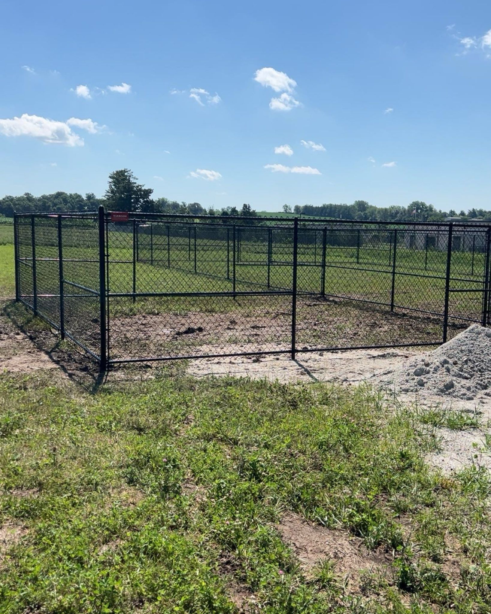 Black metal fence surrounding a dirt and grass enclosure under a blue sky.