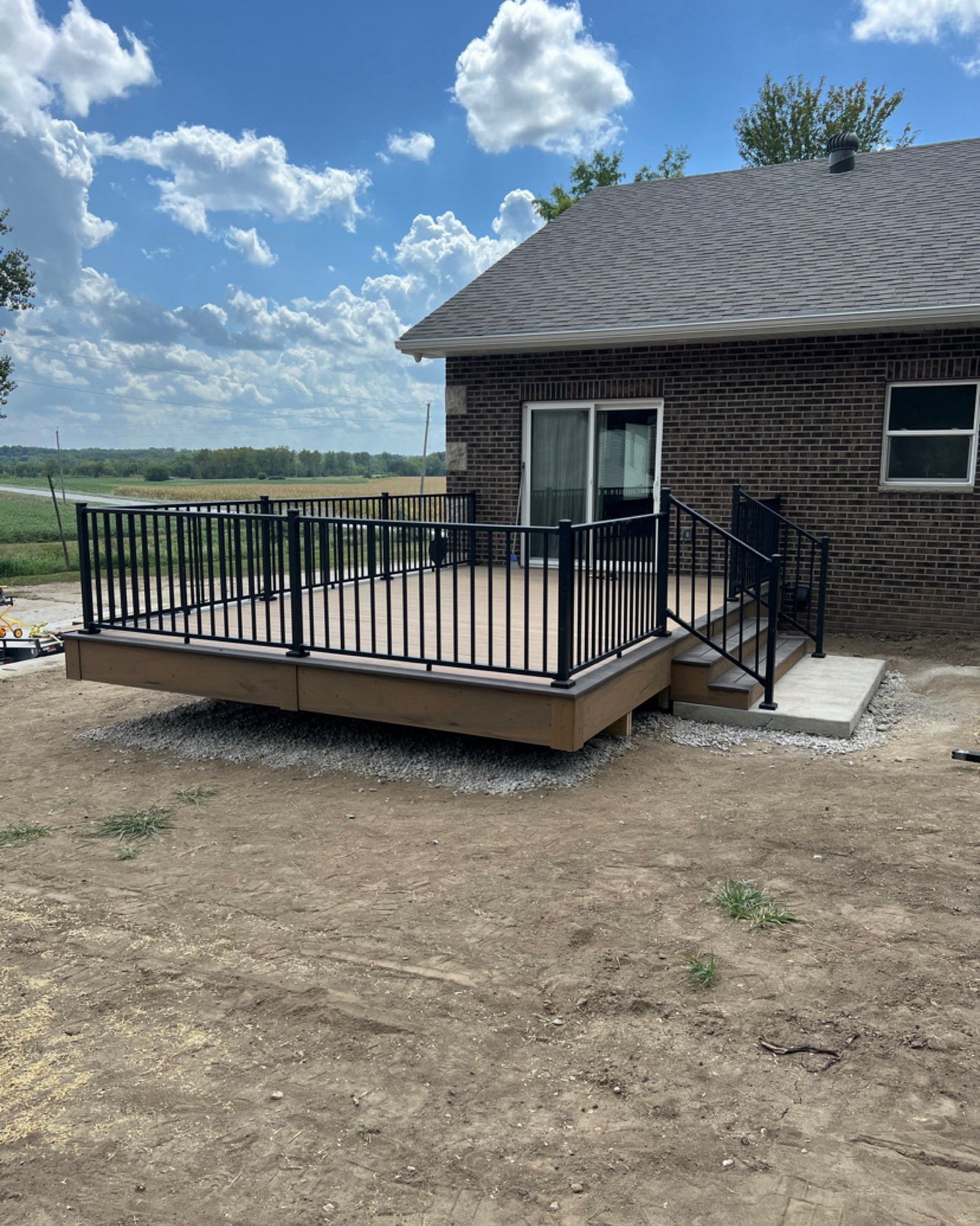 A deck with black railings and composite decking, attached to a house, against a blue sky.