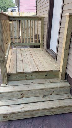 Wooden deck and stairs leading to a doorway with railings on both sides.