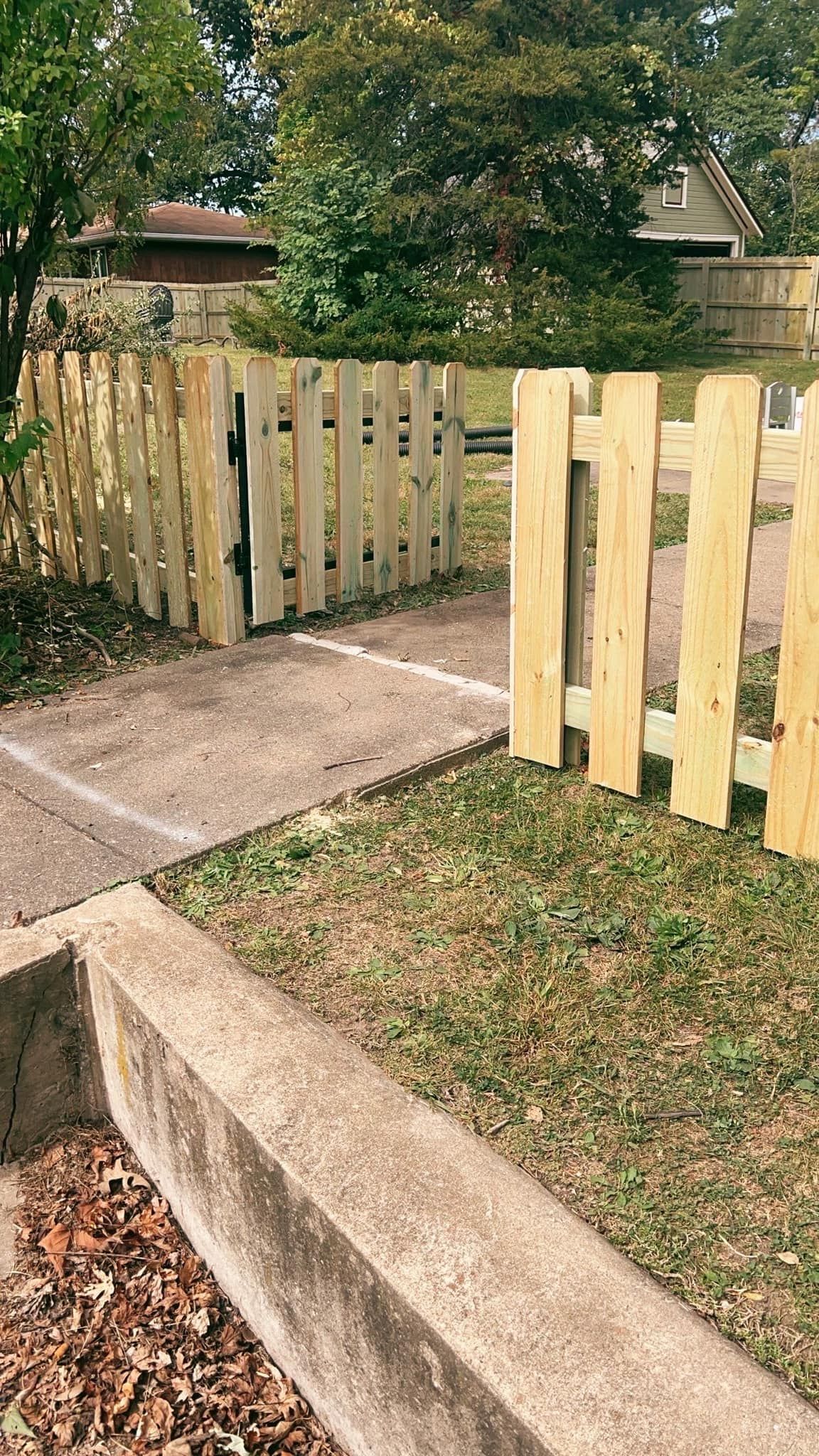 Wooden fence with open gate leading to a path in a yard.
