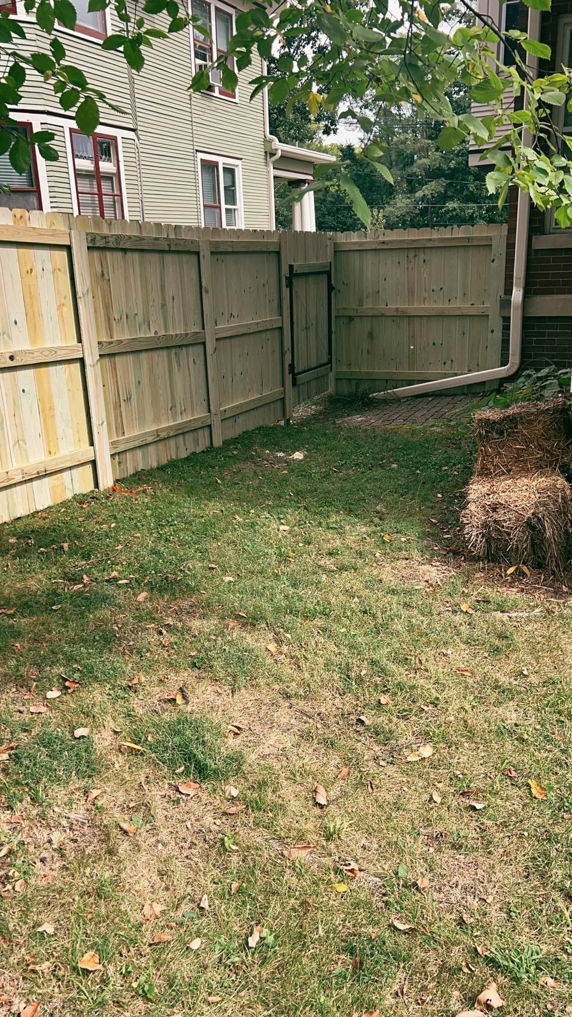 Wooden fence with a gate, in a grassy yard, adjacent to a house.
