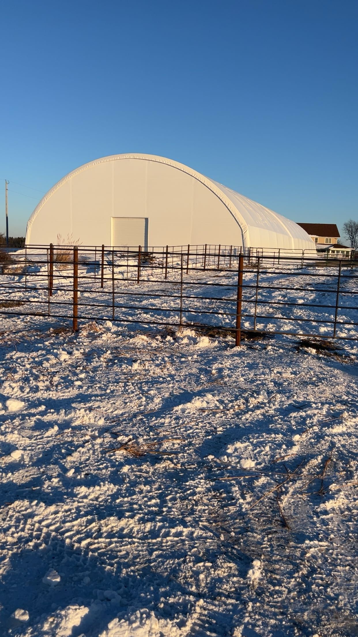 White vinyl fence on a slight incline, with houses and blue sky visible in the background.