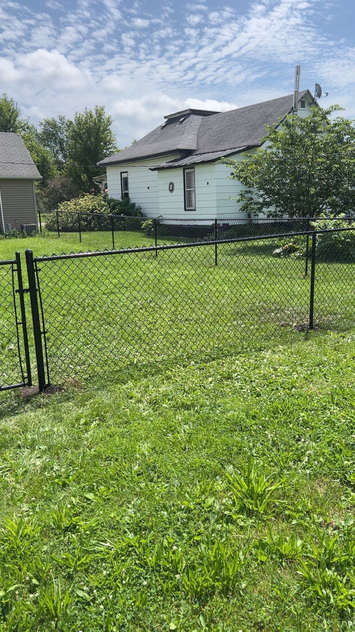 A white house with a damaged roof behind a black chain-link fence on a grassy lawn.