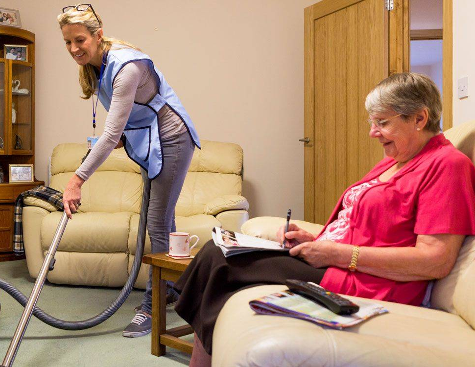 female caregiver vacuuming the home of an elderly female patient.