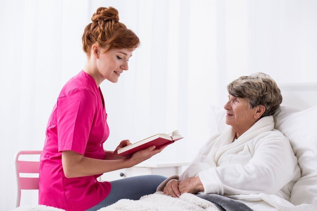 senior caregiver reading to an elderly woman in bed.