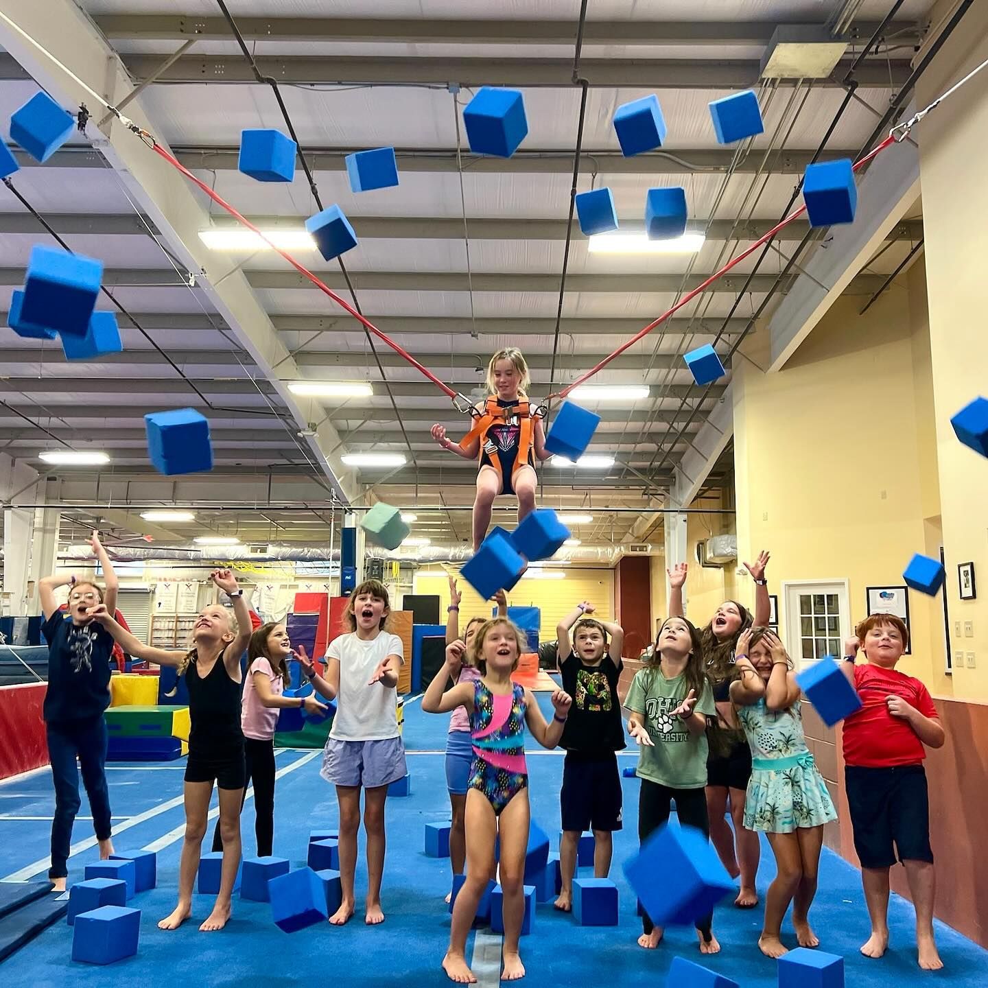 A group of children are playing with blue cubes in a gym.