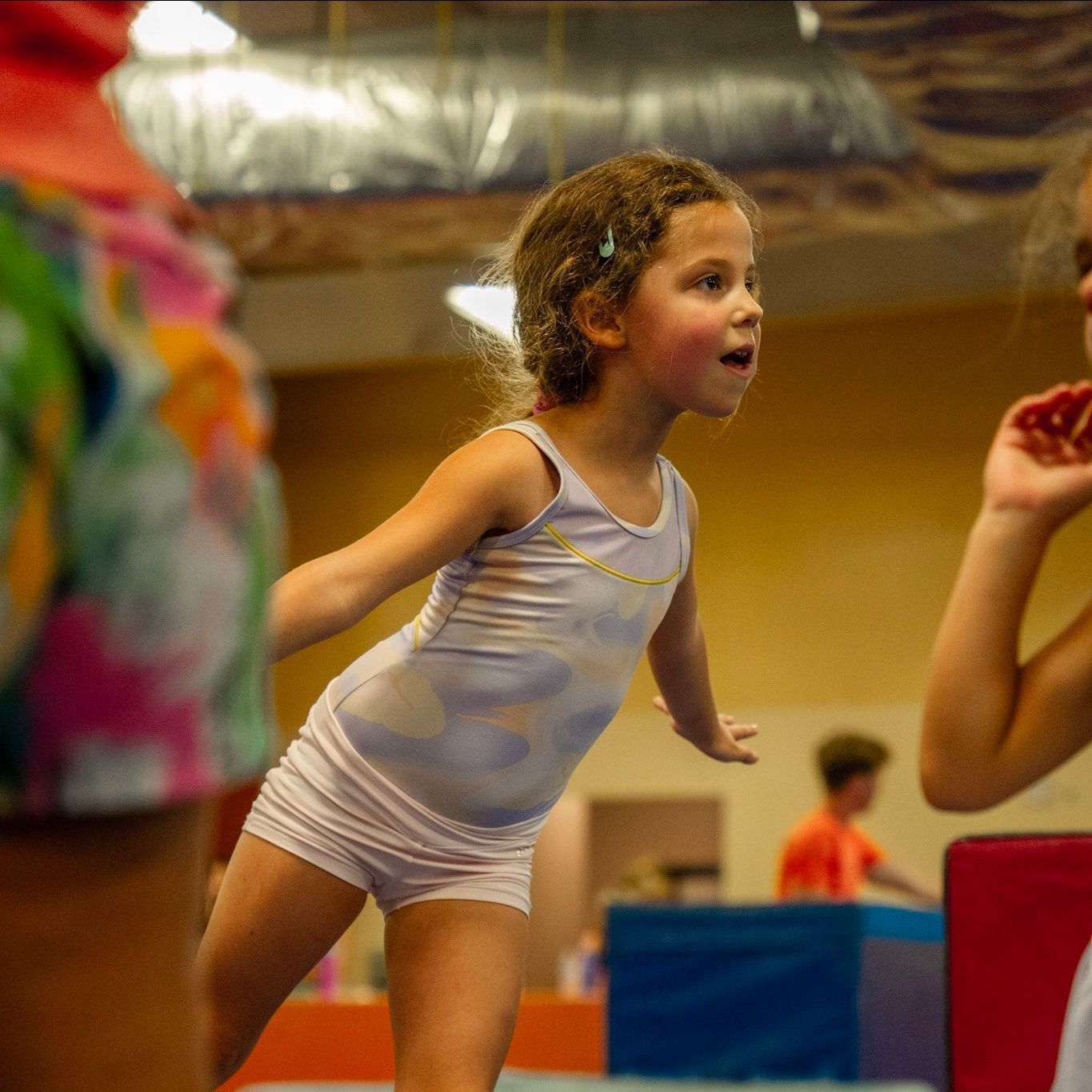 A little girl is standing on a balance beam and smiling.