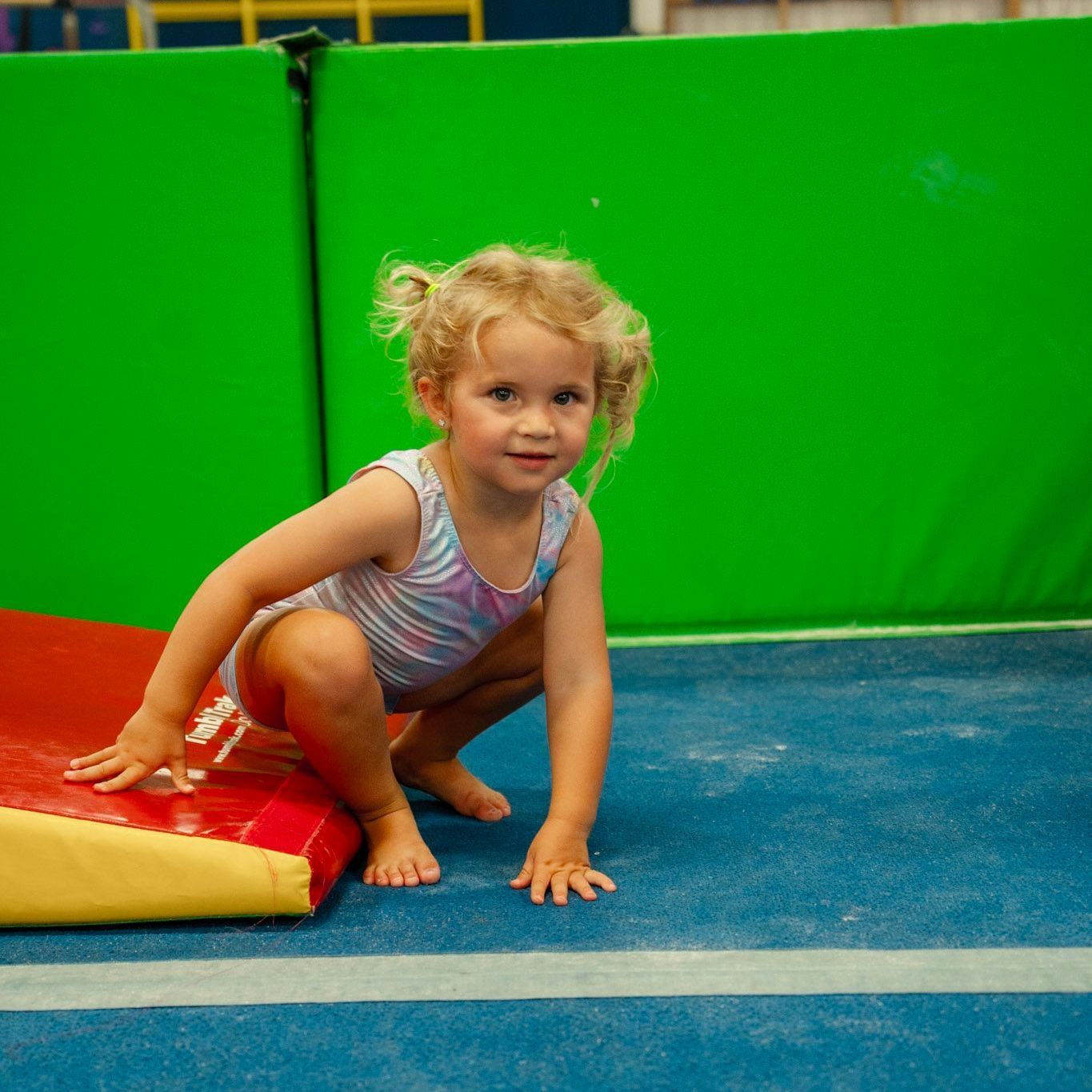 A little girl is sitting on a blue ball and smiling