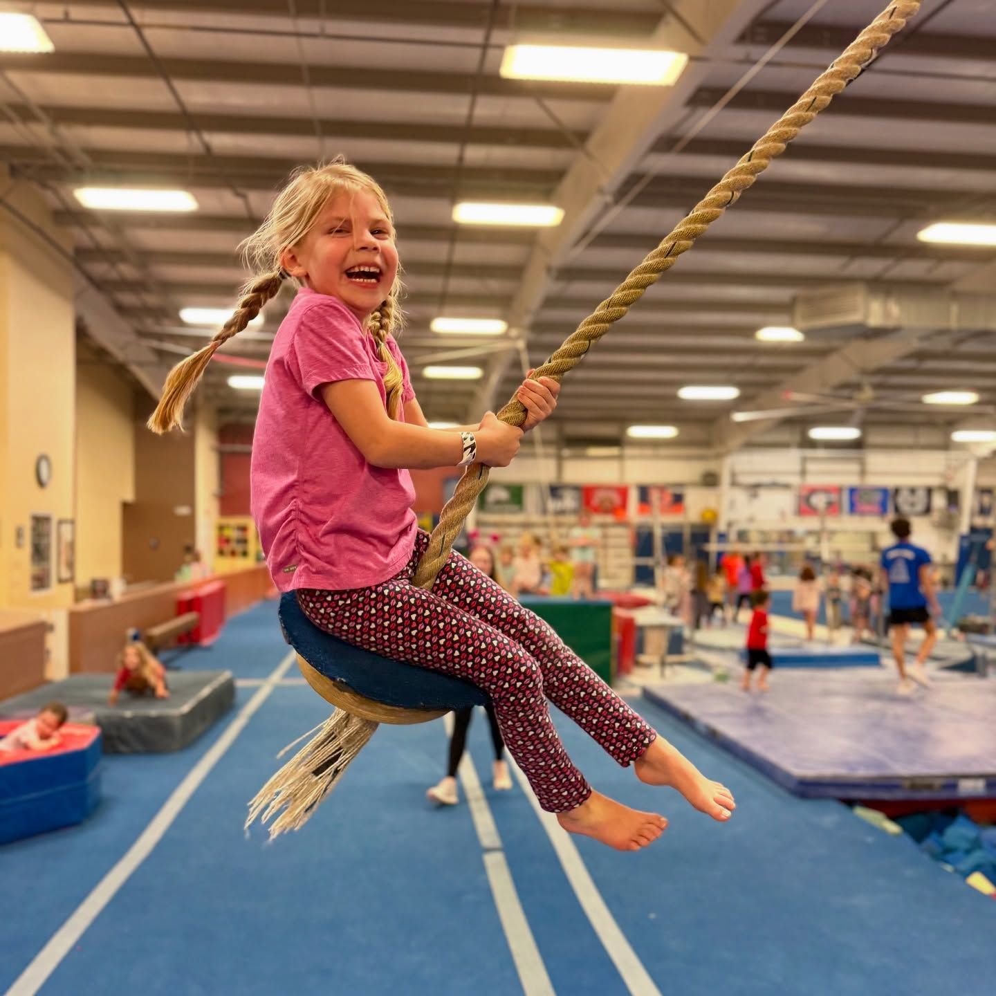 A little girl is sitting on a rope swing in a gym