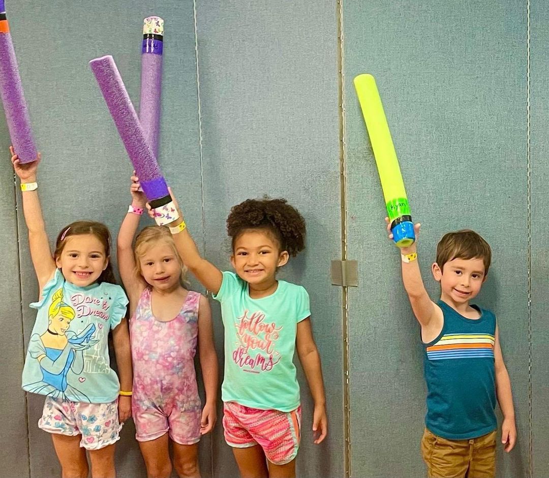 A group of children are standing next to each other holding up their foam swords.