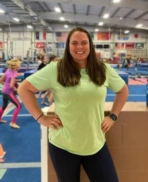 A woman in a green shirt is standing in a gym with her hands on her hips.