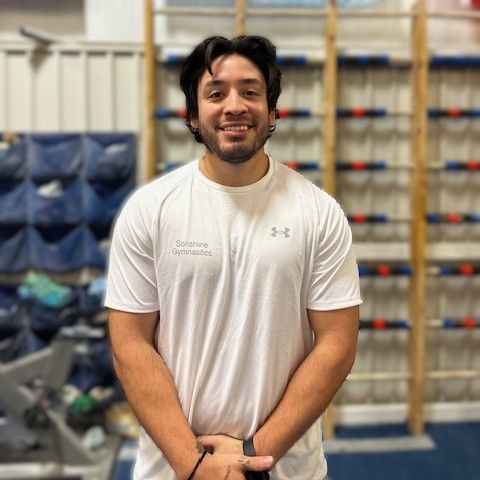 A man wearing a white under armour shirt is standing in a gym.
