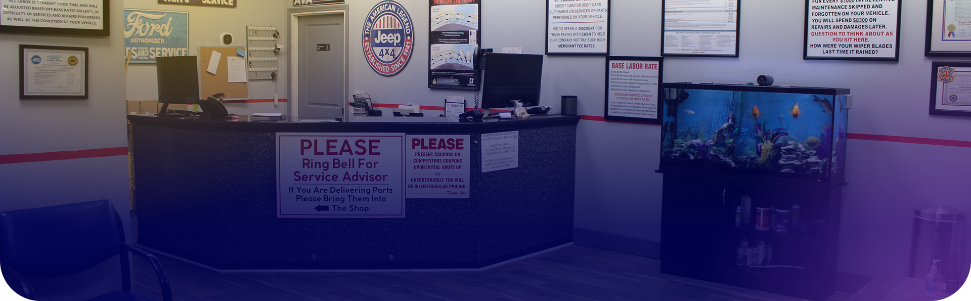 Reception desk at an auto repair shop with a fish tank, computer monitors, and informational signs on the walls. | Smithwest Service Center