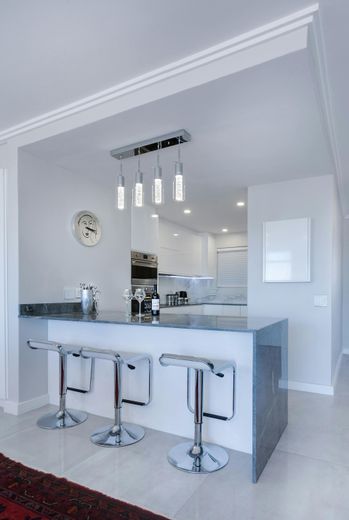 A kitchen with a bar and stools and a clock on the wall.