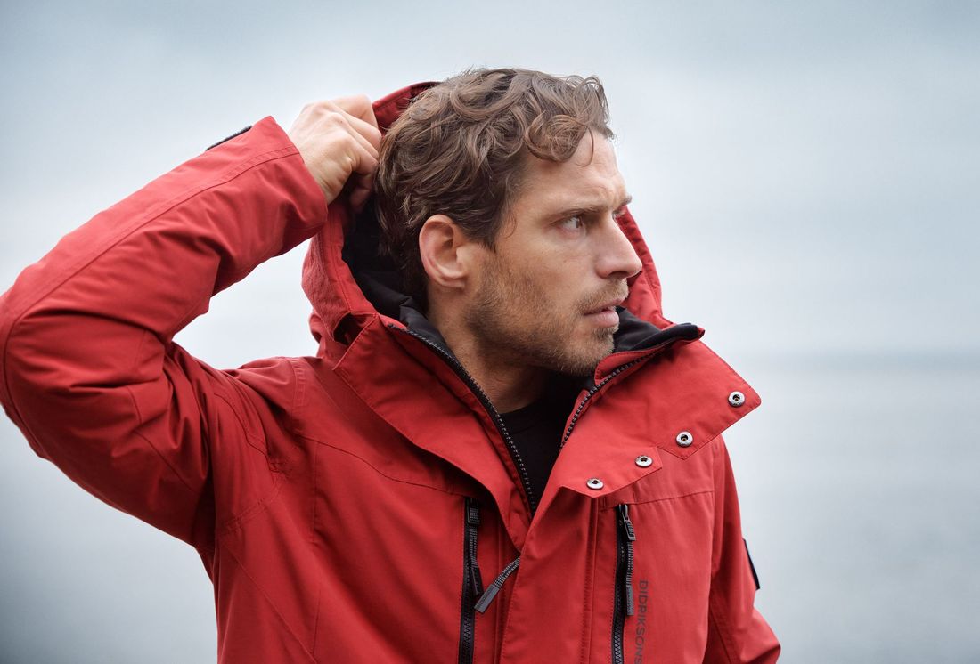Ein Mann in einer roten Jacke richtet seine Kapuze.