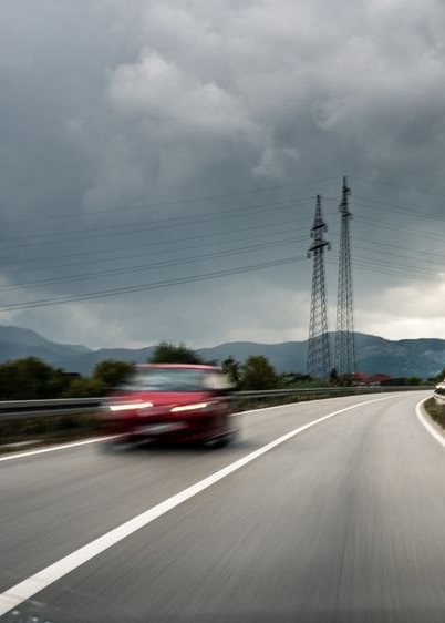 Red car blurred on a highway, under a cloudy sky with power lines in the distance.