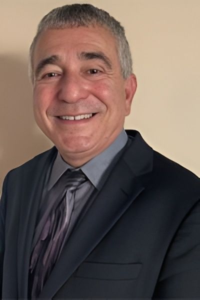 Man in a suit smiles at the camera against a neutral background.