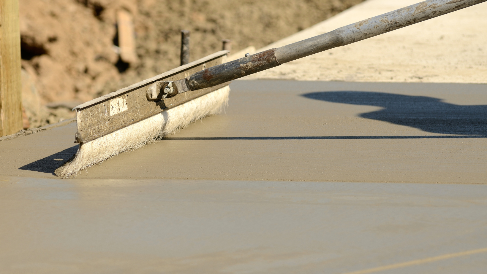 A concrete float tool smoothing freshly poured wet concrete on a construction site.