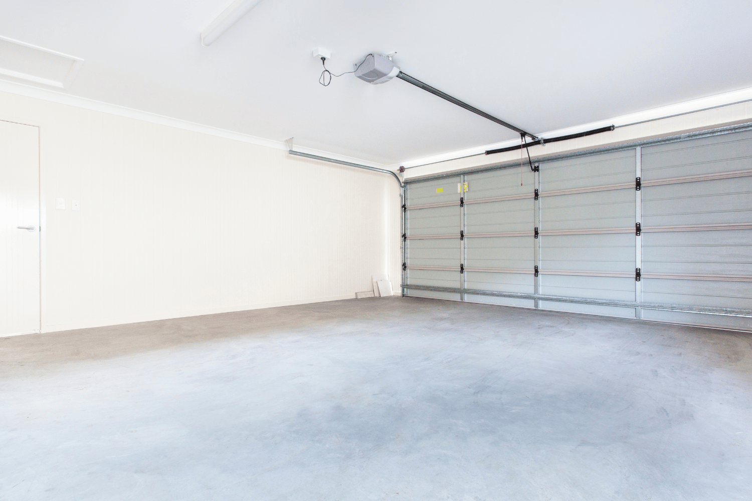 A bright, empty garage with white walls, a gray concrete floor, and a closed sectional metal garage door.