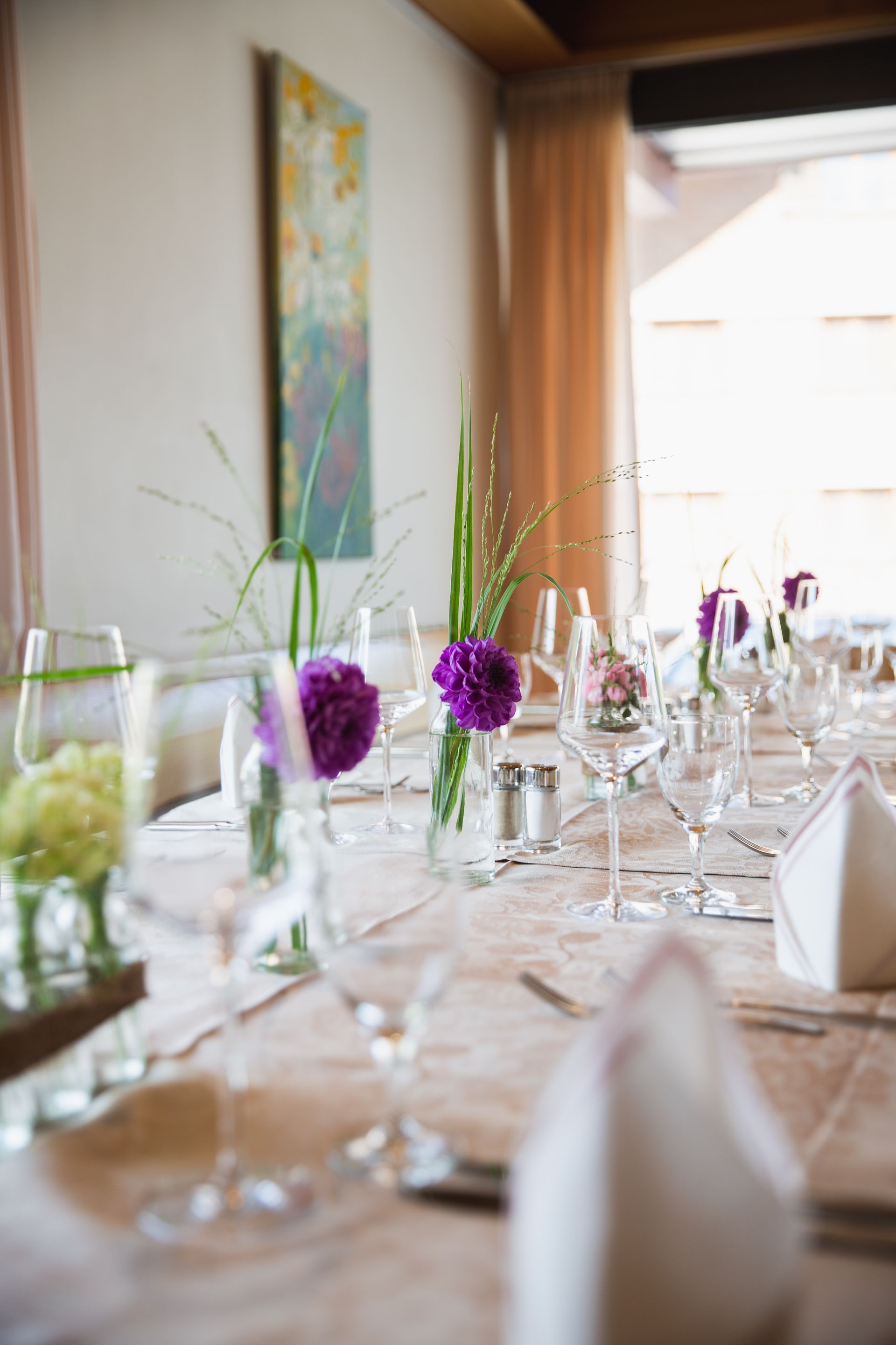Ein langer Tisch, der für einen Hochzeitsempfang mit lila Blumen in Vasen gedeckt ist.