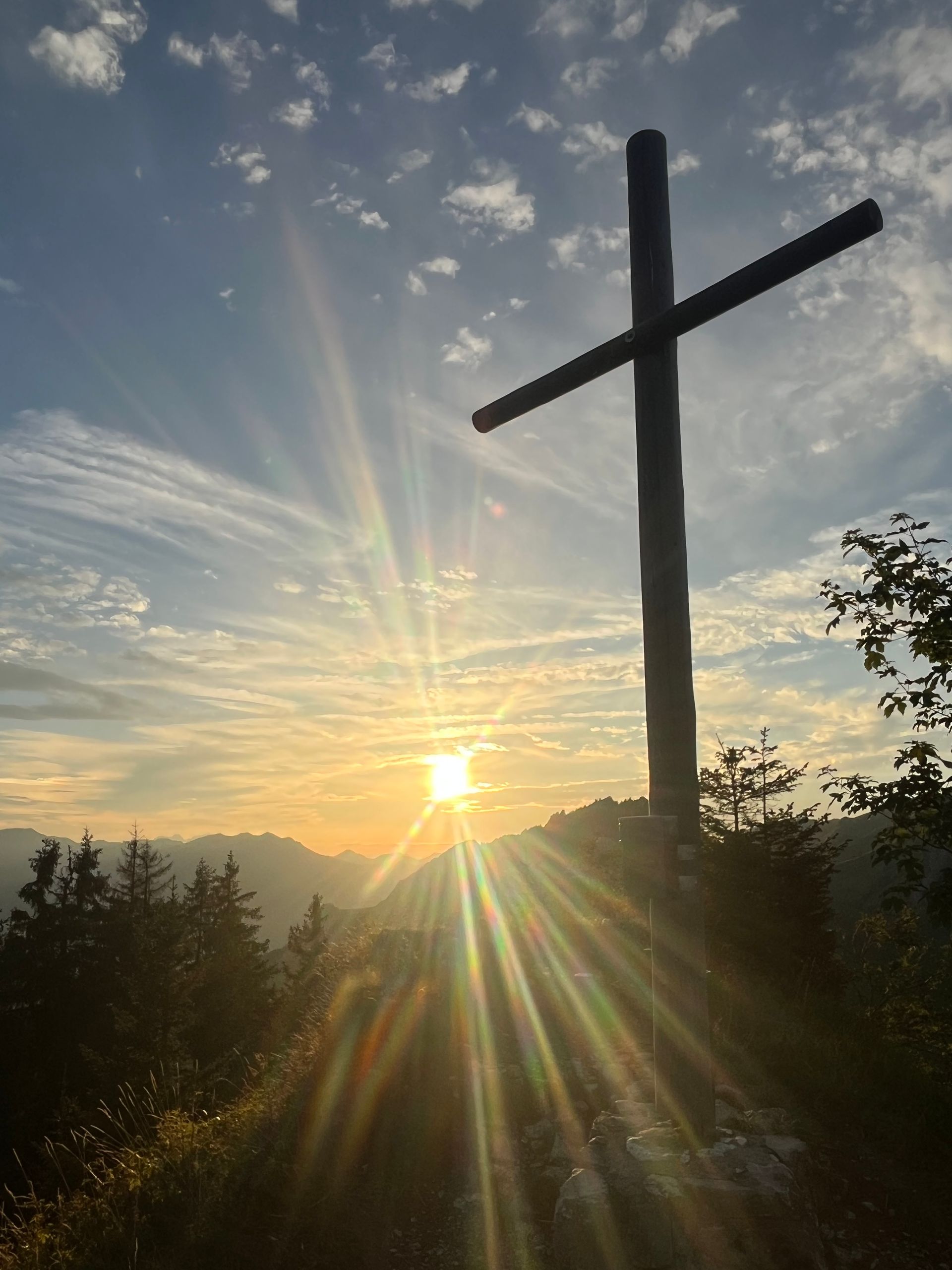 Die Sonne geht hinter einem Holzkreuz auf einem Hügel unter .